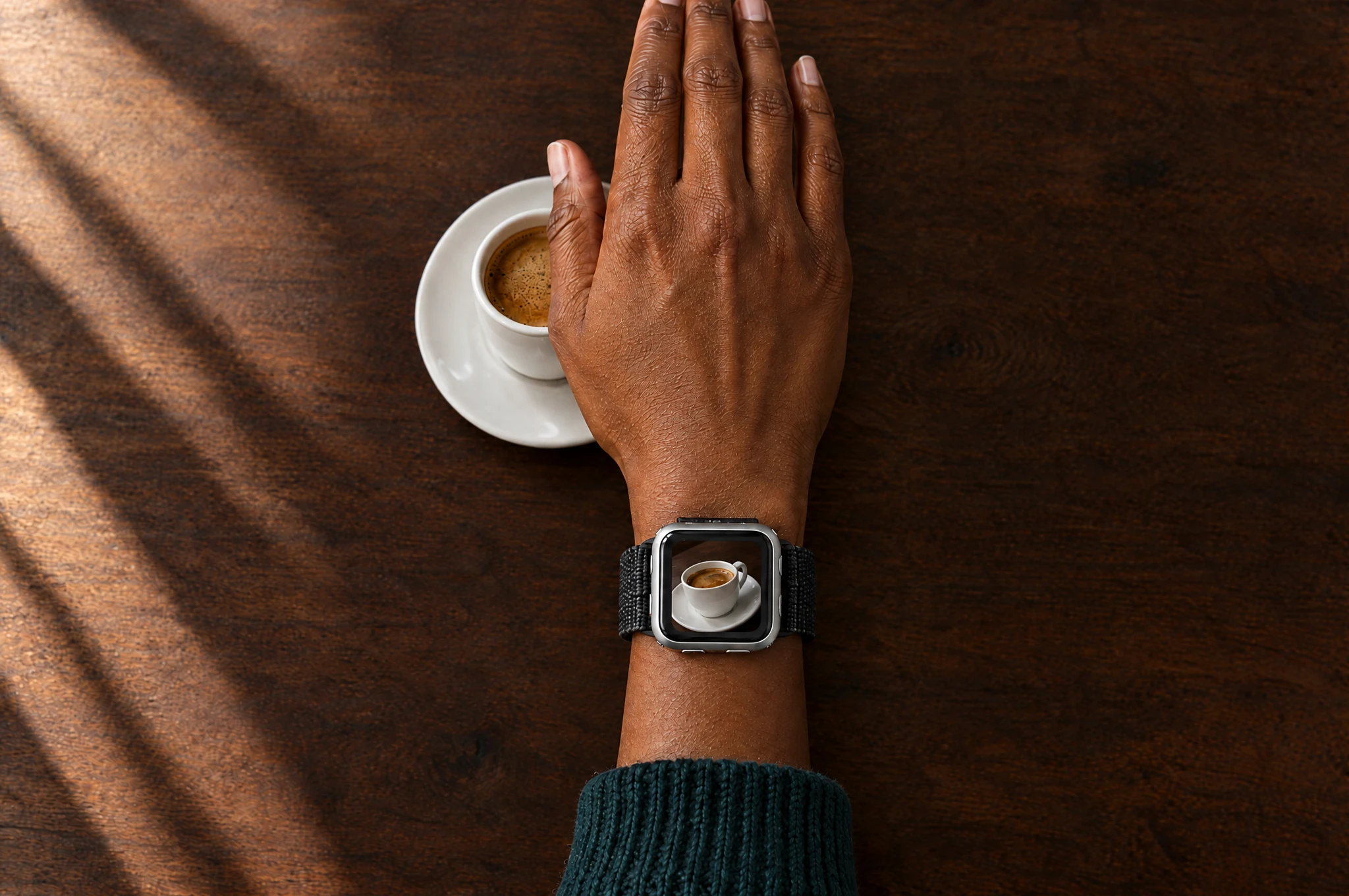 A right hand hovering over coffee, with an oblique band-camera view on the watch screen
