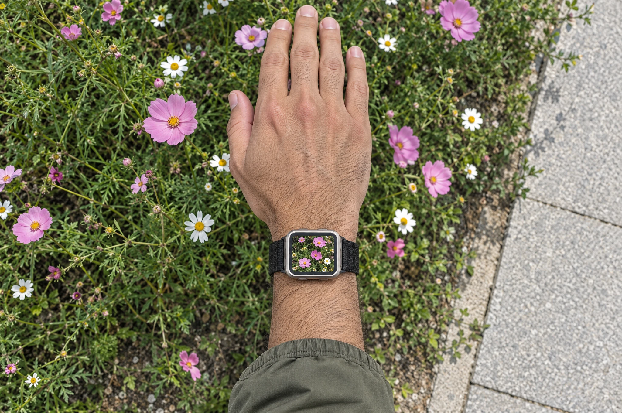 A right wrist above roadside flowers, with the flowers shown on the watch screen